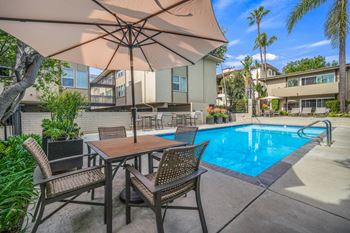 A patio with a table and chairs under an umbrella next to a pool at West Park Village, Los Angeles, 90025